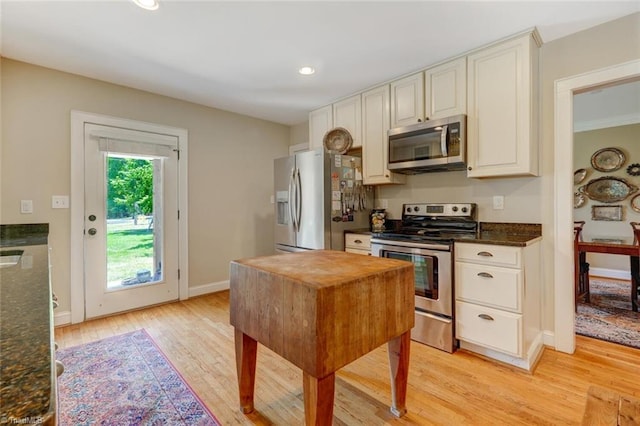 kitchen featuring appliances with stainless steel finishes, light hardwood / wood-style flooring, dark stone countertops, and white cabinets