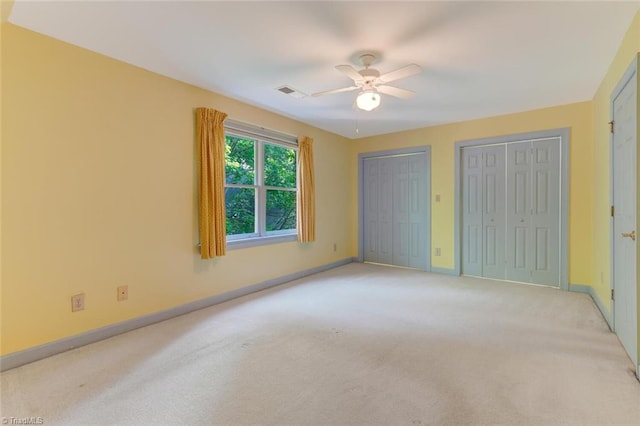 unfurnished bedroom with ceiling fan, light colored carpet, and two closets