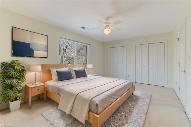 bedroom featuring ceiling fan, light carpet, and multiple closets