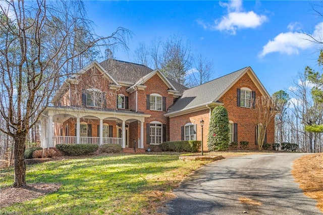 view of front of house featuring brick siding, a shingled roof, a porch, a front yard, and driveway