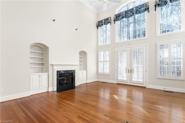 unfurnished living room with baseboards, built in shelves, wood finished floors, and a high end fireplace