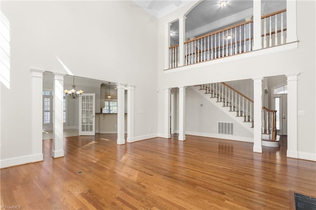 unfurnished living room with visible vents, baseboards, a chandelier, stairs, and wood finished floors