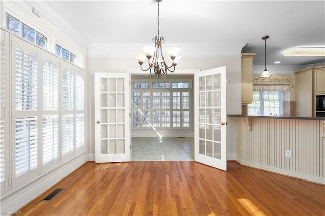 unfurnished dining area with wood finished floors, visible vents, ornamental molding, french doors, and a notable chandelier