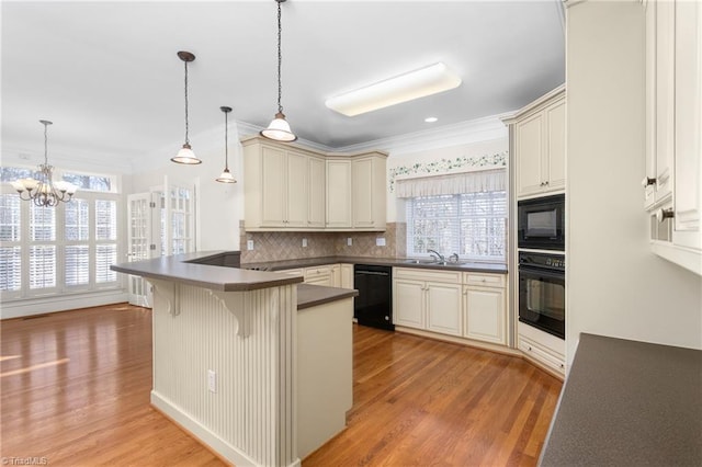 kitchen with cream cabinetry, dark countertops, black appliances, and a peninsula