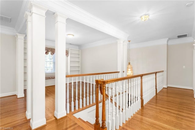 hallway with an upstairs landing, visible vents, crown molding, and wood finished floors