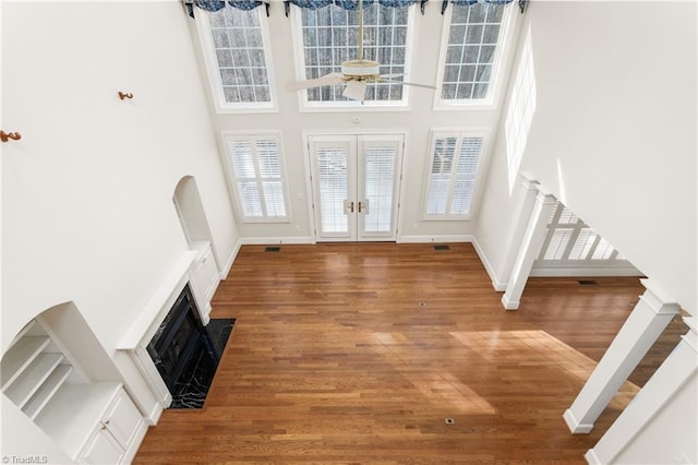 foyer with stairway, wood finished floors, a high ceiling, a fireplace with flush hearth, and french doors