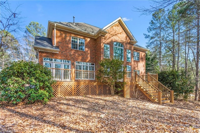 back of property with brick siding, stairway, and roof with shingles