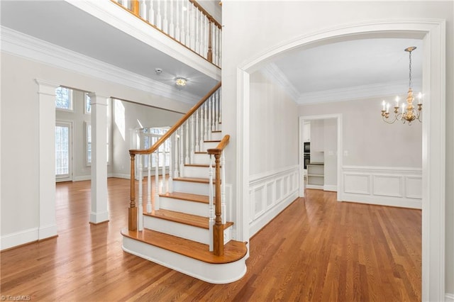 stairway with a notable chandelier, wood finished floors, arched walkways, and ornamental molding