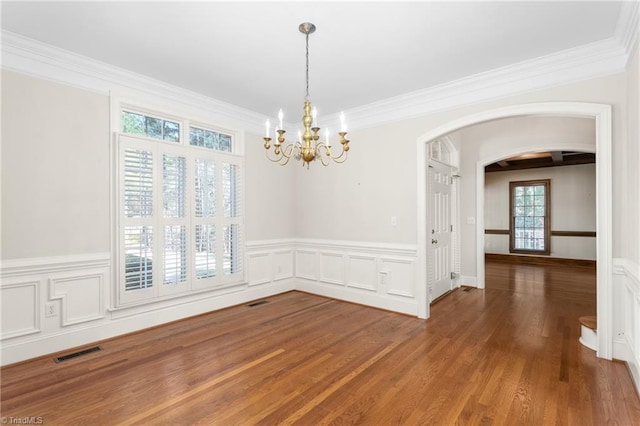 unfurnished dining area featuring visible vents, a chandelier, ornamental molding, wood finished floors, and arched walkways