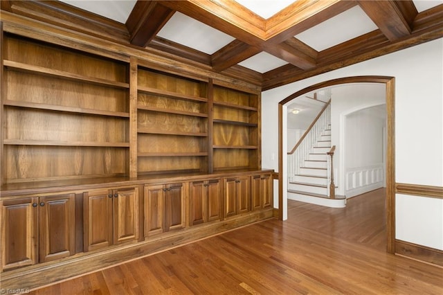 empty room with dark wood finished floors, stairs, beam ceiling, arched walkways, and coffered ceiling