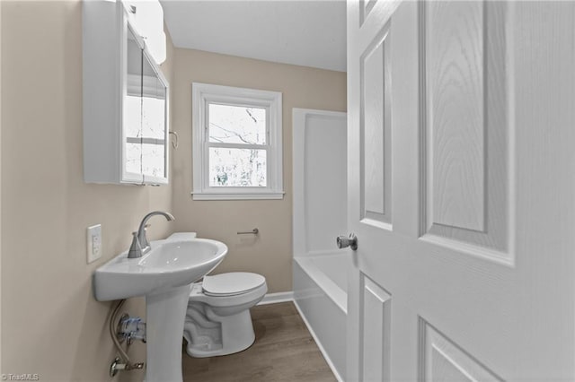 bathroom with toilet, baseboards, a washtub, and wood finished floors