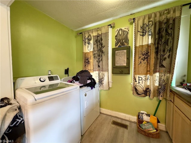 washroom featuring a textured ceiling, washer and clothes dryer, and light hardwood / wood-style flooring