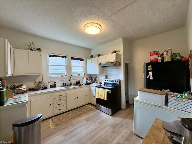 kitchen featuring tasteful backsplash, sink, black refrigerator, light hardwood / wood-style floors, and stainless steel range with electric stovetop