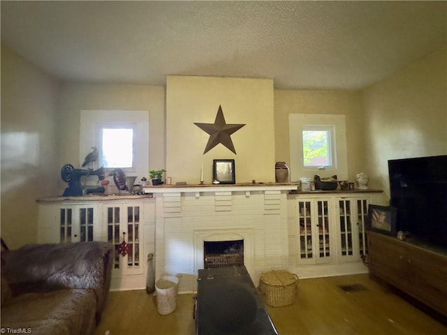 living room featuring a healthy amount of sunlight, wood-type flooring, a fireplace, and a textured ceiling