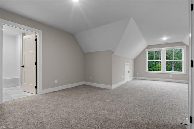 additional living space featuring vaulted ceiling and light colored carpet