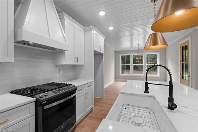 kitchen with premium range hood, hanging light fixtures, light stone countertops, white cabinets, and gas range