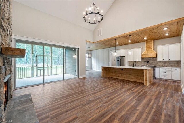 kitchen featuring appliances with stainless steel finishes, decorative light fixtures, white cabinetry, custom exhaust hood, and a center island with sink