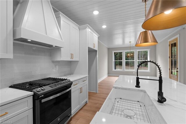 kitchen with premium range hood, light stone counters, stainless steel range with gas cooktop, pendant lighting, and white cabinets