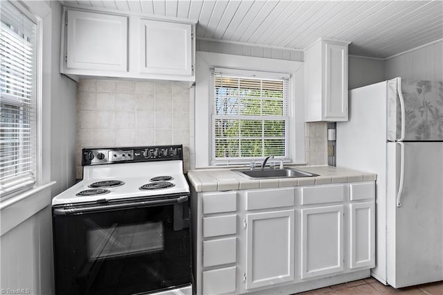 kitchen featuring range with electric stovetop, tile countertops, freestanding refrigerator, white cabinets, and a sink