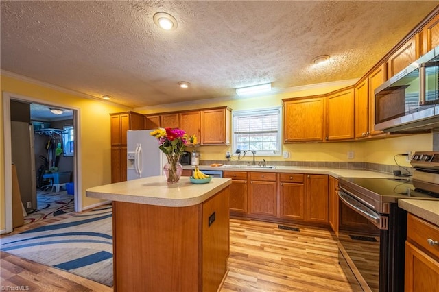 kitchen with a kitchen island, appliances with stainless steel finishes, sink, light wood-type flooring, and a textured ceiling