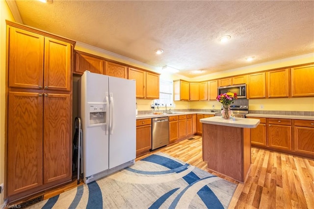 kitchen with sink, a textured ceiling, light wood-type flooring, a kitchen island, and stainless steel appliances