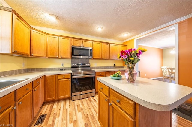 kitchen with ornamental molding, stainless steel appliances, a center island, and light hardwood / wood-style floors