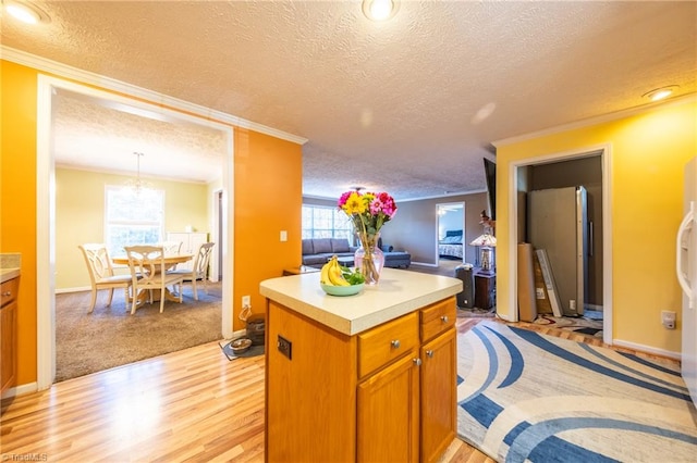 kitchen featuring ornamental molding, a textured ceiling, a kitchen island, decorative light fixtures, and light wood-type flooring