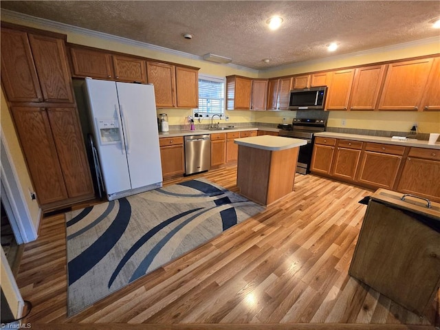 kitchen featuring a textured ceiling, ornamental molding, a kitchen island, stainless steel appliances, and light hardwood / wood-style floors