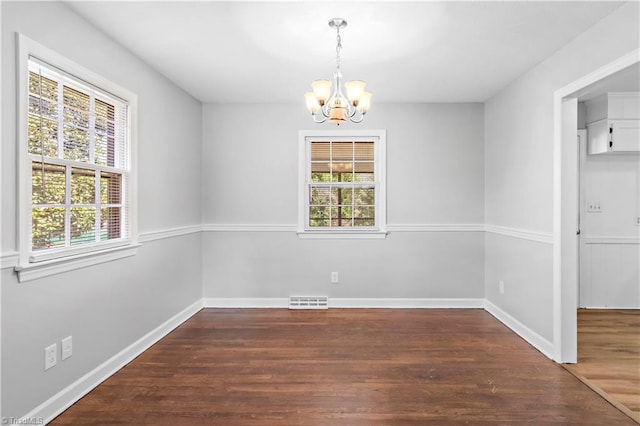 unfurnished dining area featuring a healthy amount of sunlight, dark wood-type flooring, and a chandelier