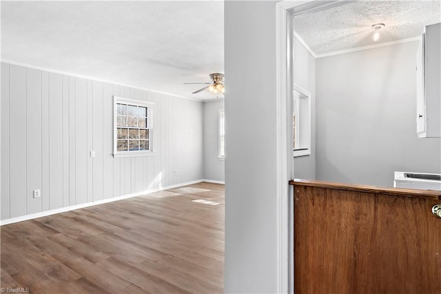 interior space featuring crown molding, wood-type flooring, a textured ceiling, a wall unit AC, and ceiling fan