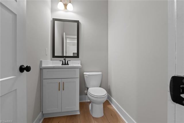 half bathroom featuring baseboards, vanity, toilet, and wood finished floors