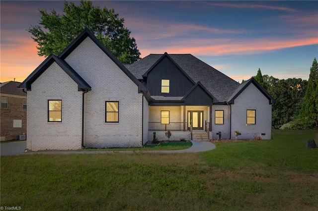 view of front of home with central AC unit, covered porch, brick siding, board and batten siding, and a yard