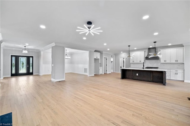 kitchen featuring crown molding, wall chimney range hood, a kitchen island with sink, and white cabinetry