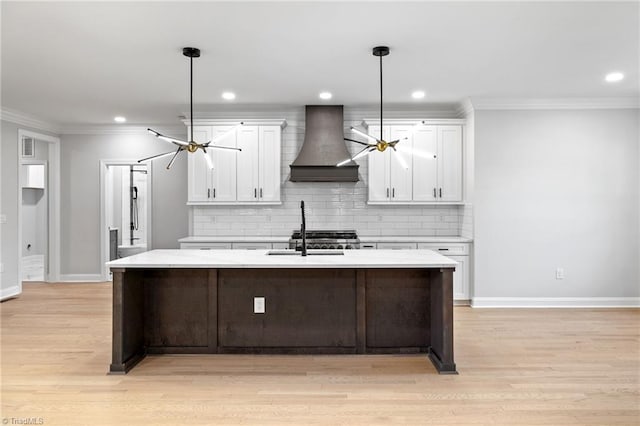 kitchen featuring white cabinets, baseboards, custom exhaust hood, and a kitchen island with sink