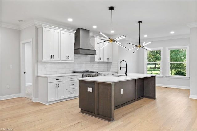 kitchen with backsplash, light countertops, wall chimney range hood, a sink, and crown molding
