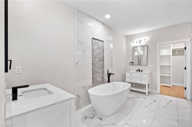 full bath featuring a sink, a walk in closet, a freestanding tub, marble finish floor, and two vanities