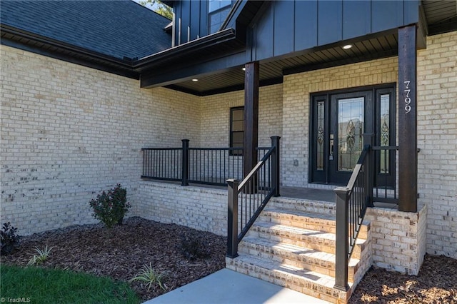 view of exterior entry with board and batten siding, covered porch, and brick siding