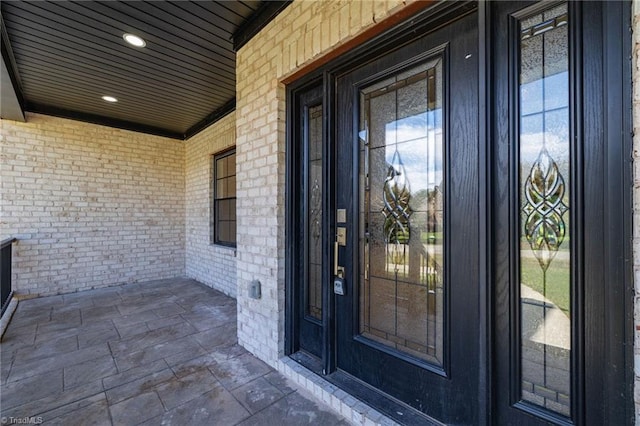 view of exterior entry with brick siding and a porch