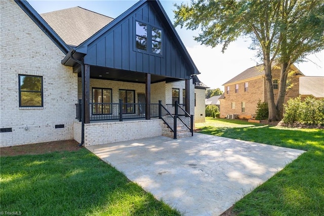 back of house with crawl space, board and batten siding, covered porch, a yard, and brick siding
