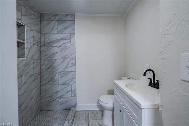 bathroom featuring vanity, ornamental molding, toilet, and a tile shower