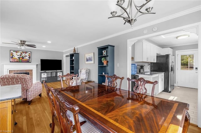 dining space featuring ceiling fan with notable chandelier, light wood-style flooring, a fireplace, and ornamental molding