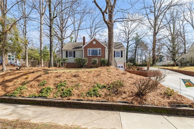 view of front facade featuring brick siding, an attached garage, fence, a chimney, and driveway