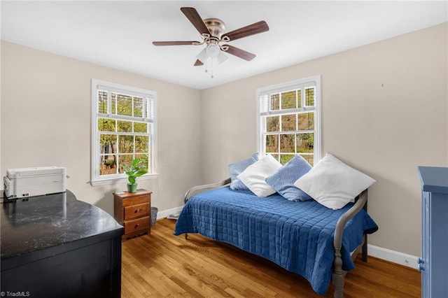 bedroom with multiple windows, light wood-style floors, and baseboards