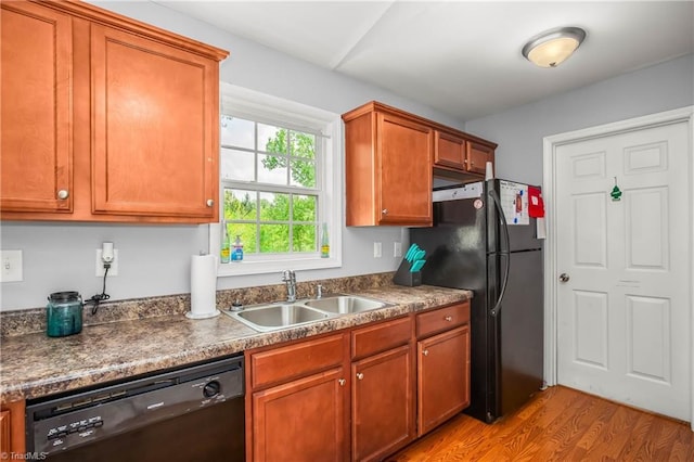 kitchen with brown cabinetry, black appliances, dark countertops, a sink, and light wood-type flooring