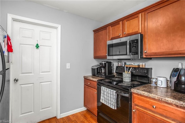 kitchen with brown cabinetry, black appliances, light wood-style flooring, baseboards, and dark countertops