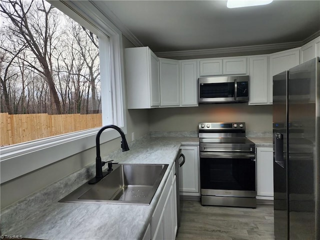 kitchen with crown molding, sink, black appliances, light hardwood / wood-style flooring, and white cabinets