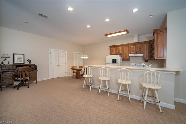 3913 Katie Dr, Greensboro, NC 27410 - kitchen with under cabinet range hood, visible vents, brown cabinetry, white refrigerator with ice dispenser, and light colored carpet