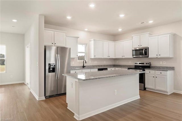 kitchen with light stone countertops, white cabinetry, stainless steel appliances, light hardwood / wood-style floors, and a kitchen island