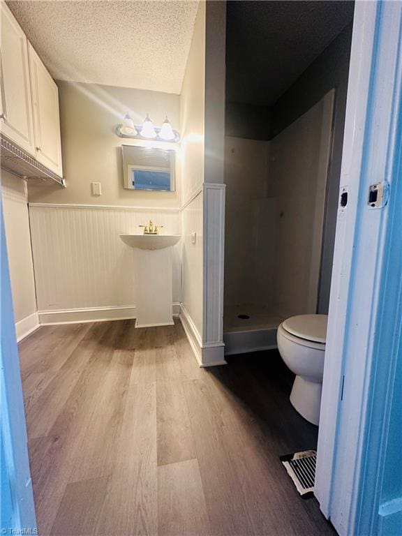 bathroom featuring walk in shower, a textured ceiling, sink, toilet, and hardwood / wood-style flooring