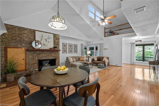 4701 Brock Dr, Hurdle Mills, NC 27541 - dining area featuring a fireplace, light wood-type flooring, ceiling fan, high vaulted ceiling, and a textured ceiling